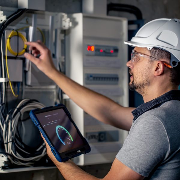 Man, an electrical technician working in a switchboard with fuses, uses a tablet. Man, an electrical technician working in a switchboard with fuses. Installation and connection of electrical equipment.